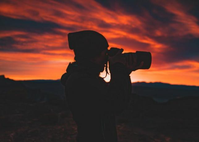 Osoba, ktorá drží fotoaparát pri západe slnka